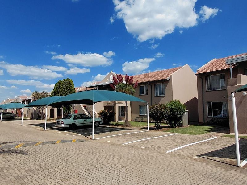 Exterior view of an apartment complex featuring paved parking areas with shade cloth carports and well-maintained building facades.