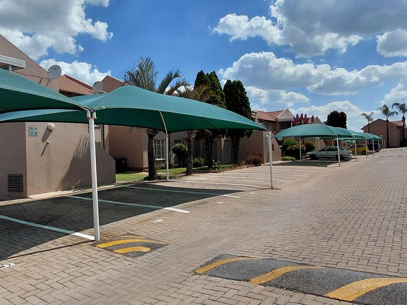 Exterior view of the apartment complex featuring a paved driveway with multiple covered parking bays and shade cloth structures.