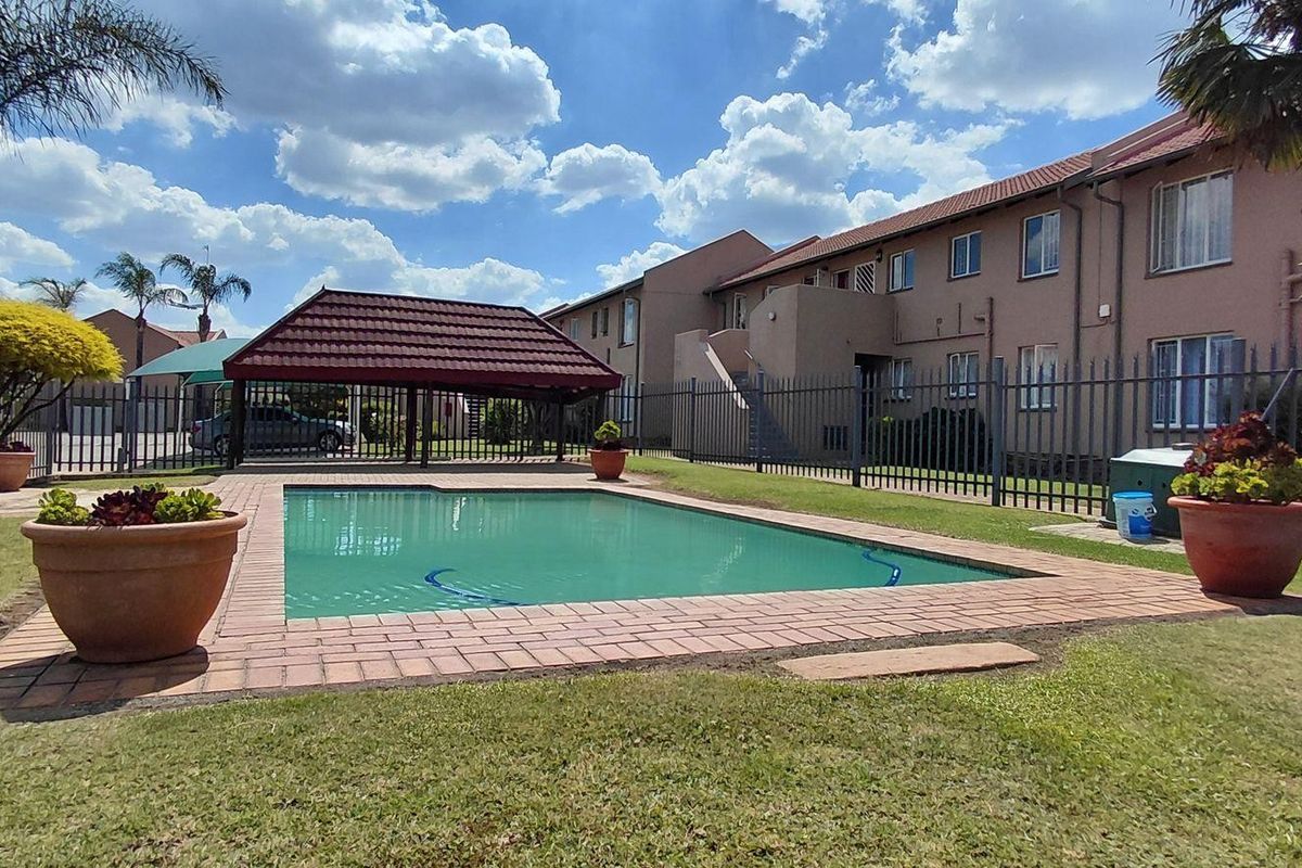 Communal outdoor area featuring a swimming pool with brick coping, a covered lapa, and established lawn within a secure fenced complex.