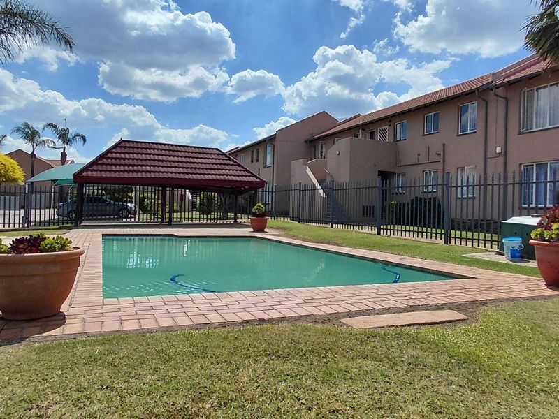 Communal outdoor area featuring a swimming pool with brick coping, a covered lapa, and established lawn within a secure fenced complex.