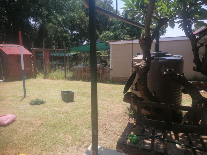 A backyard garden area featuring a water storage tank, a small shed, and a metal support structure, with lawn space and mature trees.