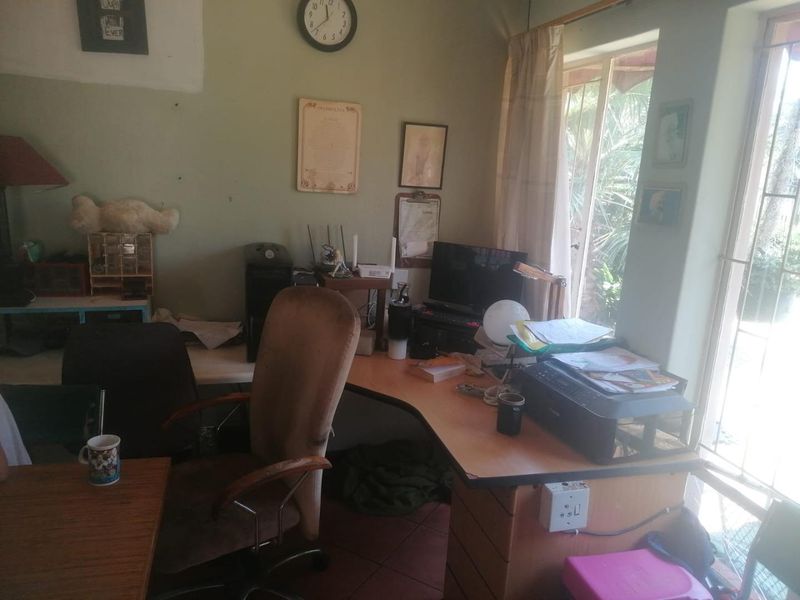 A functional home office space featuring tiled flooring and a large window with security bars, offering natural light and garden views.