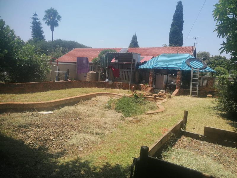 Rear garden view featuring a brick retaining wall, tiled roof dwelling, and outdoor patio area requiring significant landscaping and maintenance.