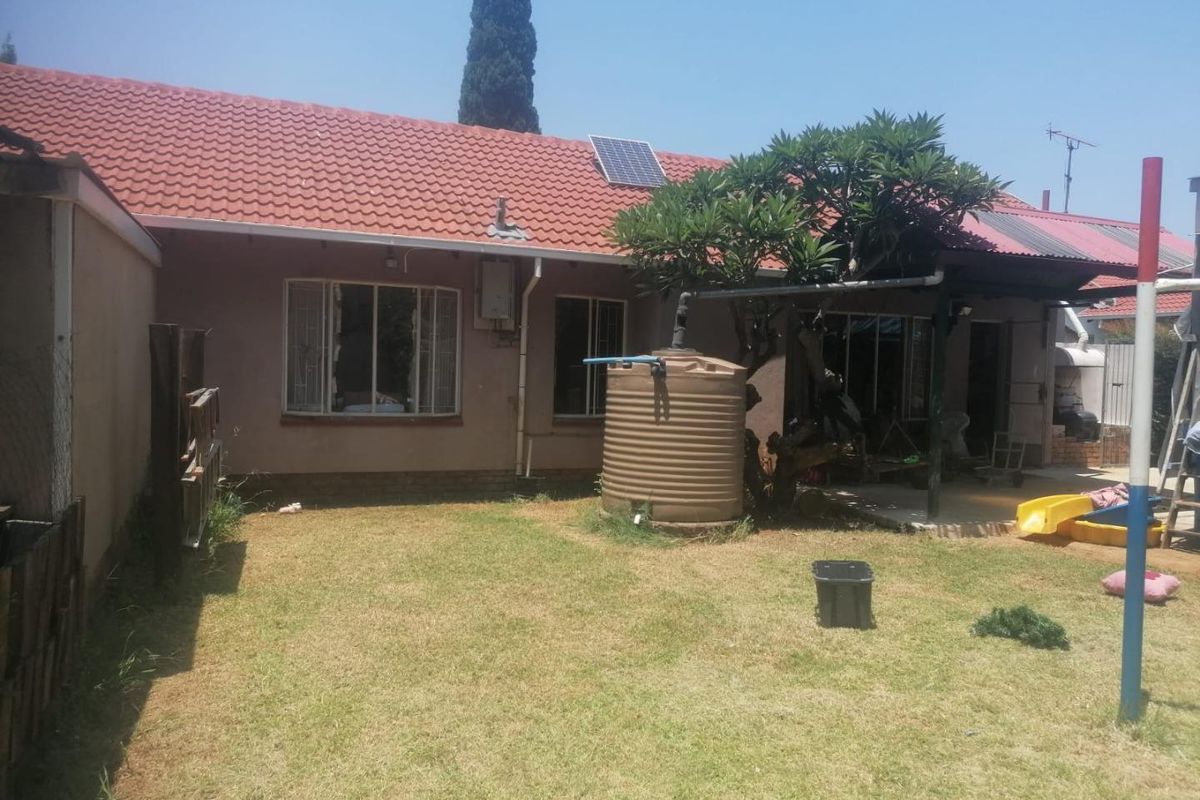 Rear view of the house featuring a tiled roof, solar panel, water storage tank, and a covered patio area overlooking the garden.