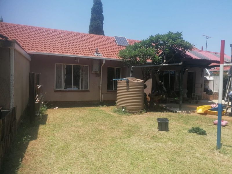 Rear view of the house featuring a tiled roof, solar panel, water storage tank, and a covered patio area overlooking the garden.
