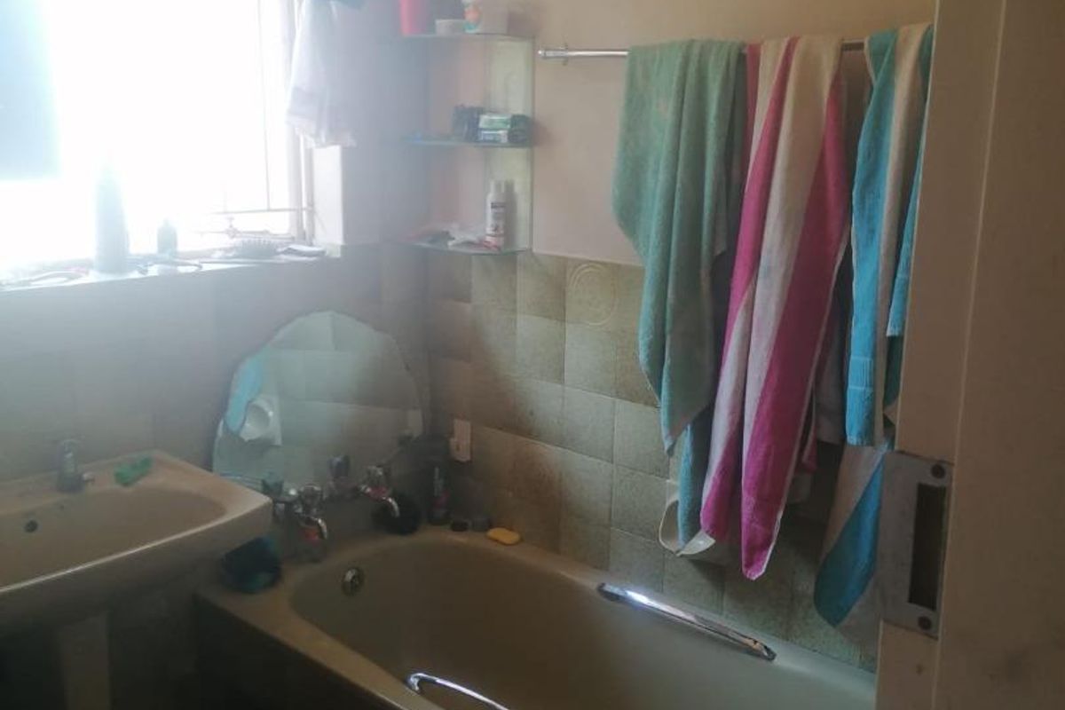 A dated bathroom featuring a bathtub, pedestal basin, and tiled splashback, requiring modernization to improve its overall aesthetic and functionality.