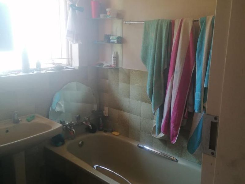 A dated bathroom featuring a bathtub, pedestal basin, and tiled splashback, requiring modernization to improve its overall aesthetic and functionality.