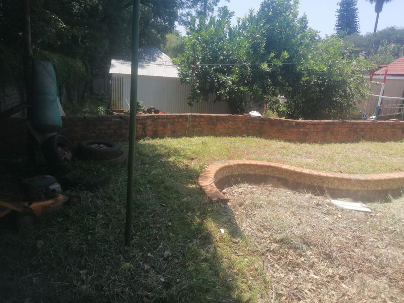 Outdoor pool area featuring a brick retaining wall and garden space, currently requiring significant maintenance and landscaping to restore its potential.