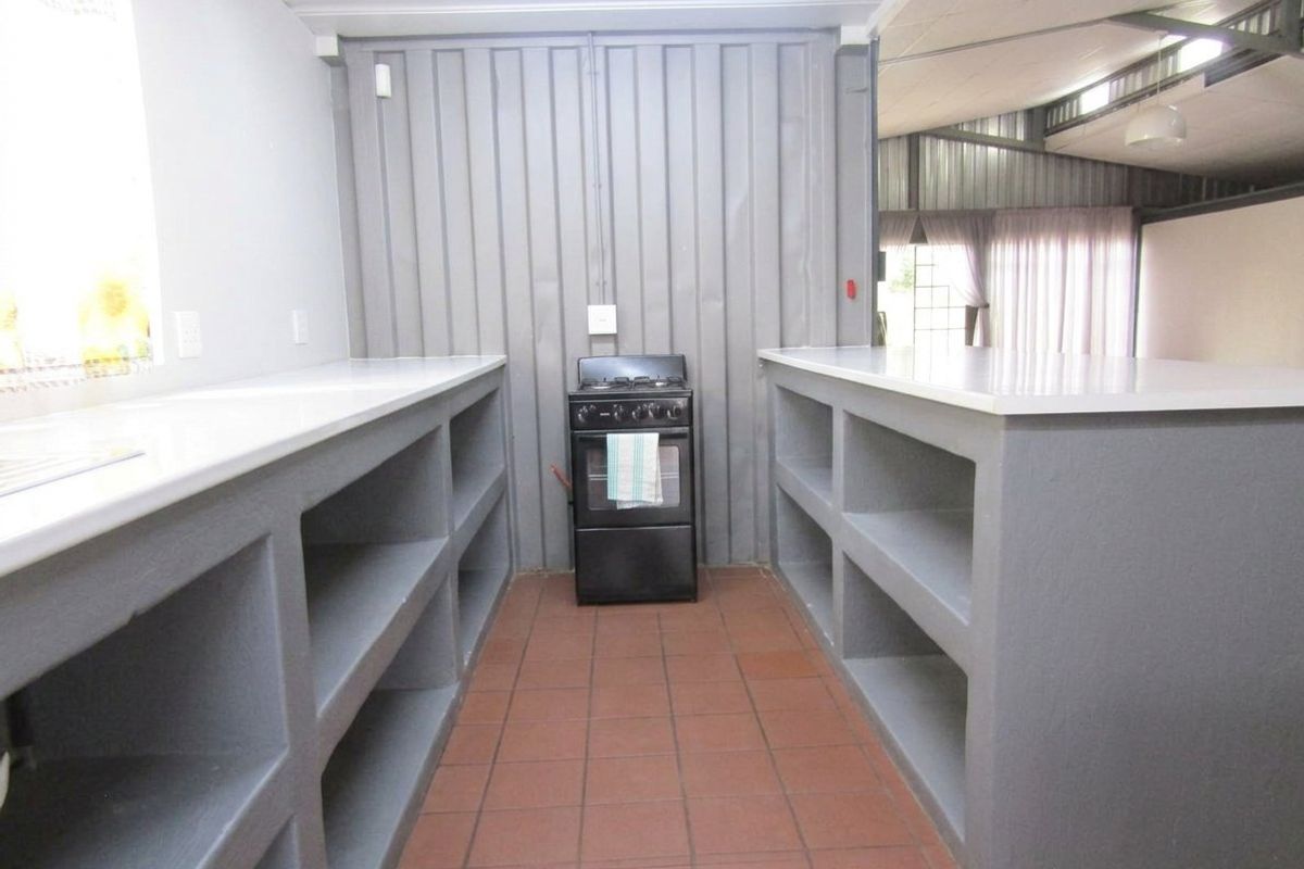 A functional kitchen area featuring built-in concrete shelving, tiled flooring, and a freestanding stove, set within a structure with corrugated metal wall finishes.
