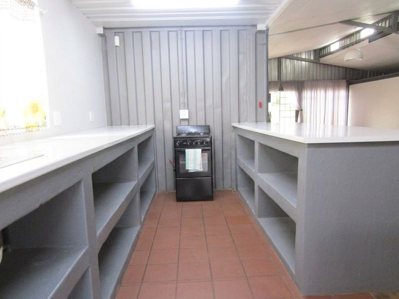 A functional kitchen area featuring built-in concrete shelving, tiled flooring, and a freestanding stove, set within a structure with corrugated metal wall finishes.