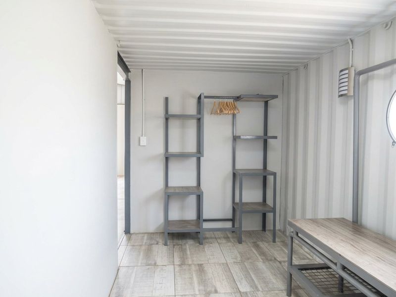 A minimalist bedroom space featuring industrial-style corrugated metal walls and ceiling, tiled flooring, and a unique circular window.