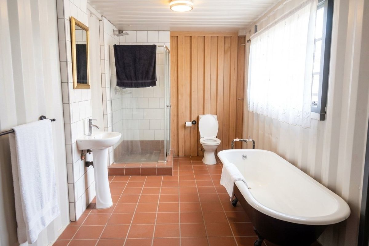 A well-lit bathroom featuring a freestanding clawfoot bathtub, a separate glass-enclosed shower, a pedestal sink, and a combination of tiled and timber wall finishes.