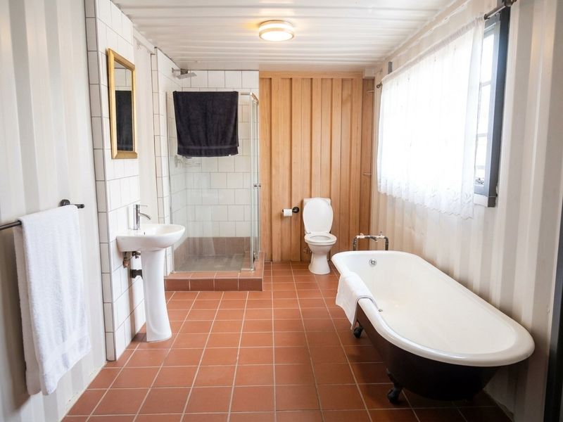 A well-lit bathroom featuring a freestanding clawfoot bathtub, a separate glass-enclosed shower, a pedestal sink, and a combination of tiled and timber wall finishes.