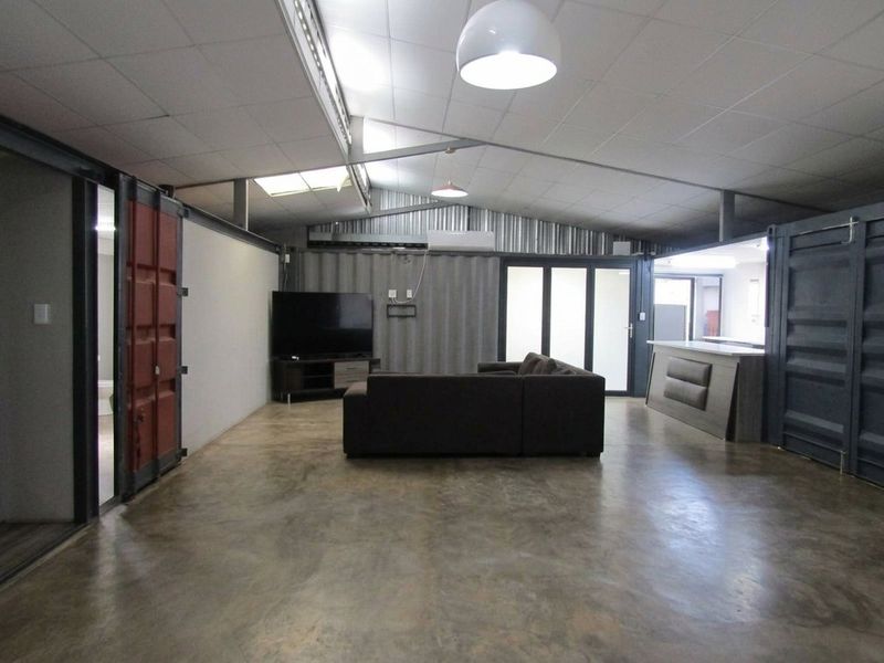Spacious open-plan living area featuring industrial design elements, including shipping container walls, polished concrete flooring, and a built-in bar counter.
