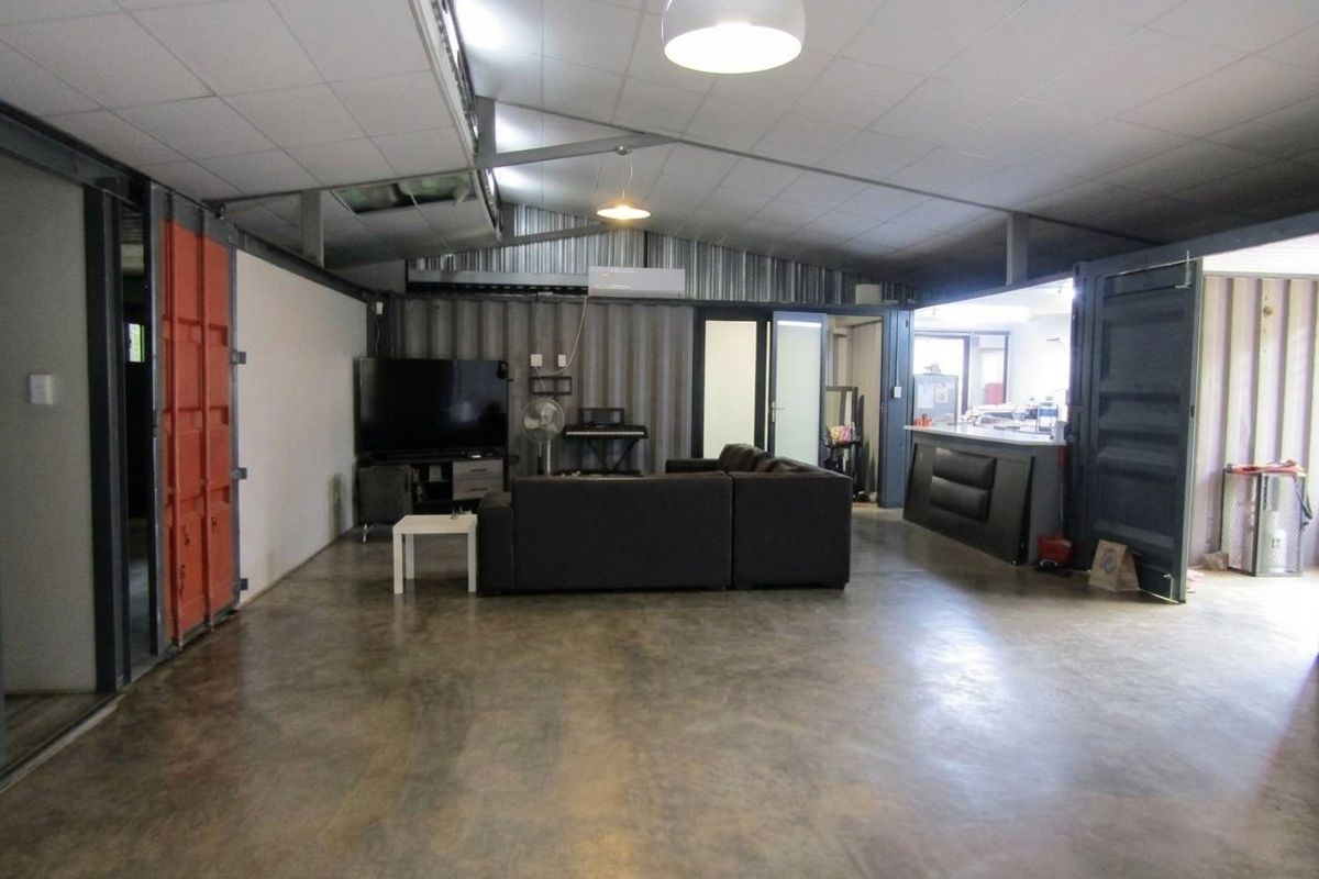 Spacious open-plan living area featuring industrial-style corrugated metal walls, polished concrete floors, and exposed steel structural elements with an integrated breakfast bar.