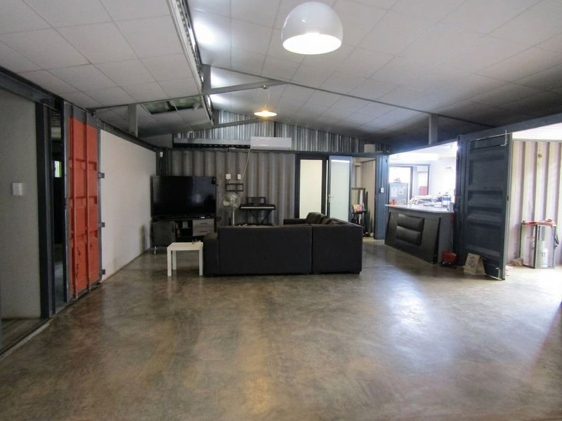 Spacious open-plan living area featuring industrial-style corrugated metal walls, polished concrete floors, and exposed steel structural elements with an integrated breakfast bar.