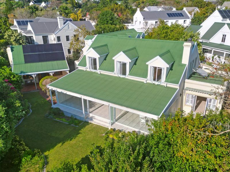 Aerial view of a residential property featuring a green corrugated metal roof, solar panels, dormer windows, and a spacious covered patio overlooking the garden.
