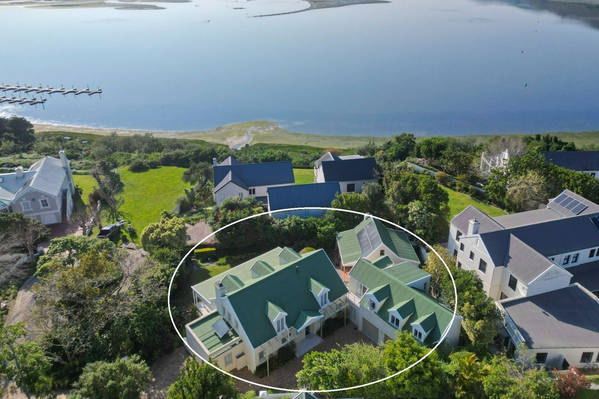 Aerial view of a multi-structure residential property featuring green metal roofing, dormer windows, and solar panels, situated in a scenic coastal estate setting.