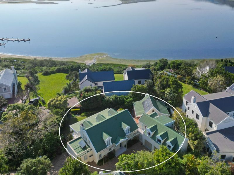 Aerial view of a multi-structure residential property featuring green metal roofing, dormer windows, and solar panels, situated in a scenic coastal estate setting.