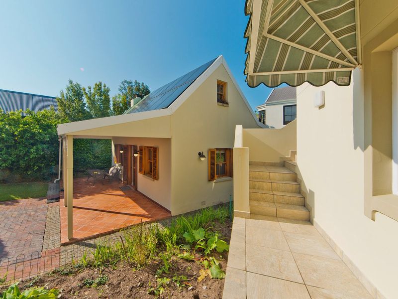 Rear exterior view featuring a tiled patio, external staircase, solar panels on the roof, and timber window shutters.