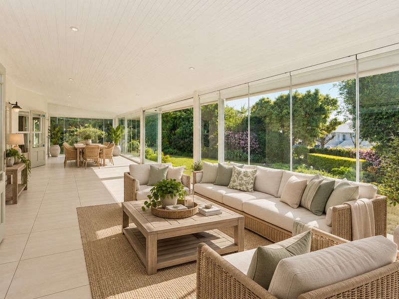 A bright and spacious enclosed patio featuring large glass sliding doors, tiled flooring, and a clean tongue and groove ceiling overlooking the garden.