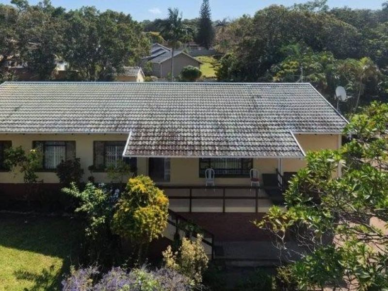 Aerial view of the rear elevation featuring a tiled roof, covered patio with timber railing, and established garden surroundings.