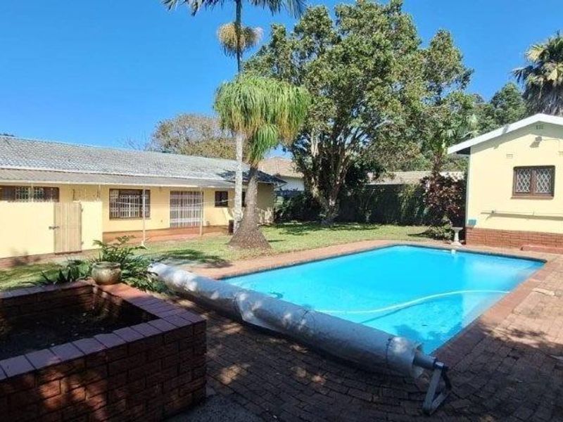 Rear exterior view featuring a swimming pool, brick paved patio area, and established garden space with a detached outbuilding.