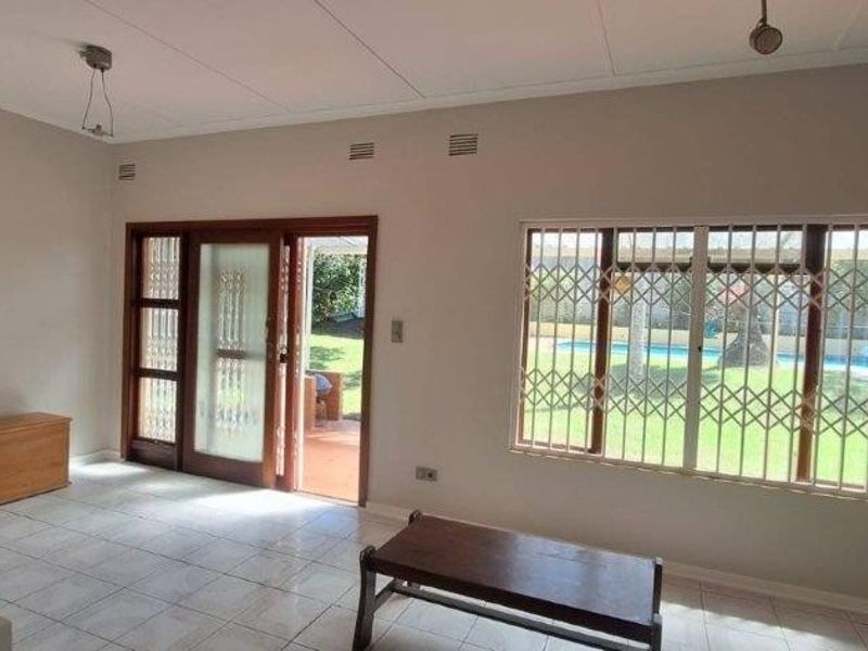 Spacious living area featuring tiled flooring, security bars on windows, and direct access to the outdoor patio and pool area.