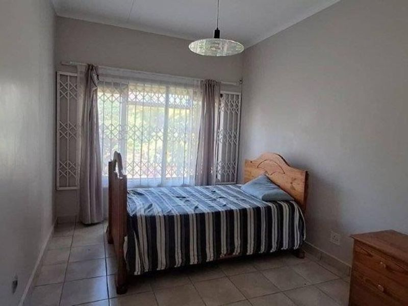 A standard bedroom featuring tiled flooring, a large window with security gates, and a central ceiling light fixture.