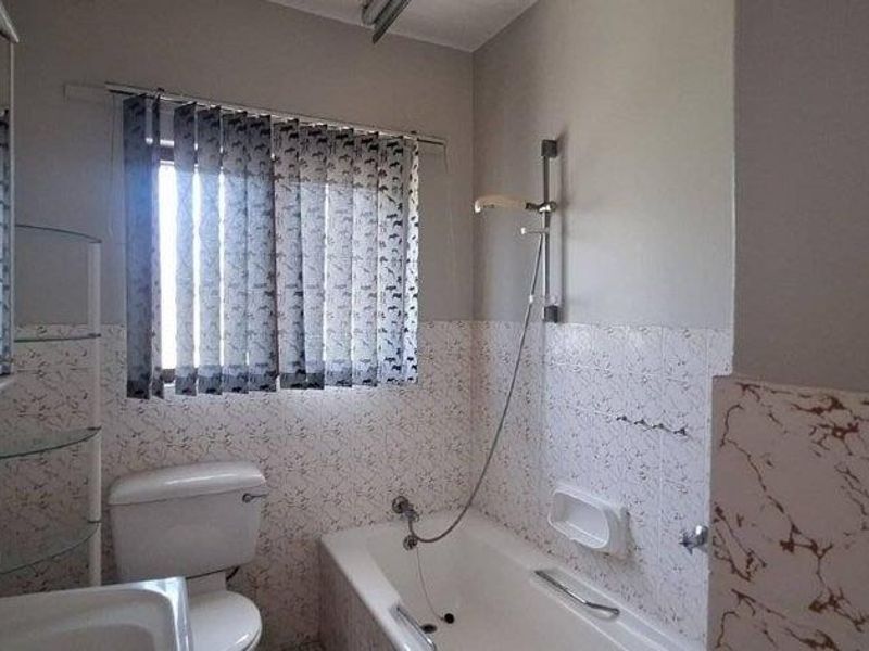 A functional bathroom featuring a bathtub with a handheld shower attachment, a toilet, and a vanity mirror cabinet with integrated storage.