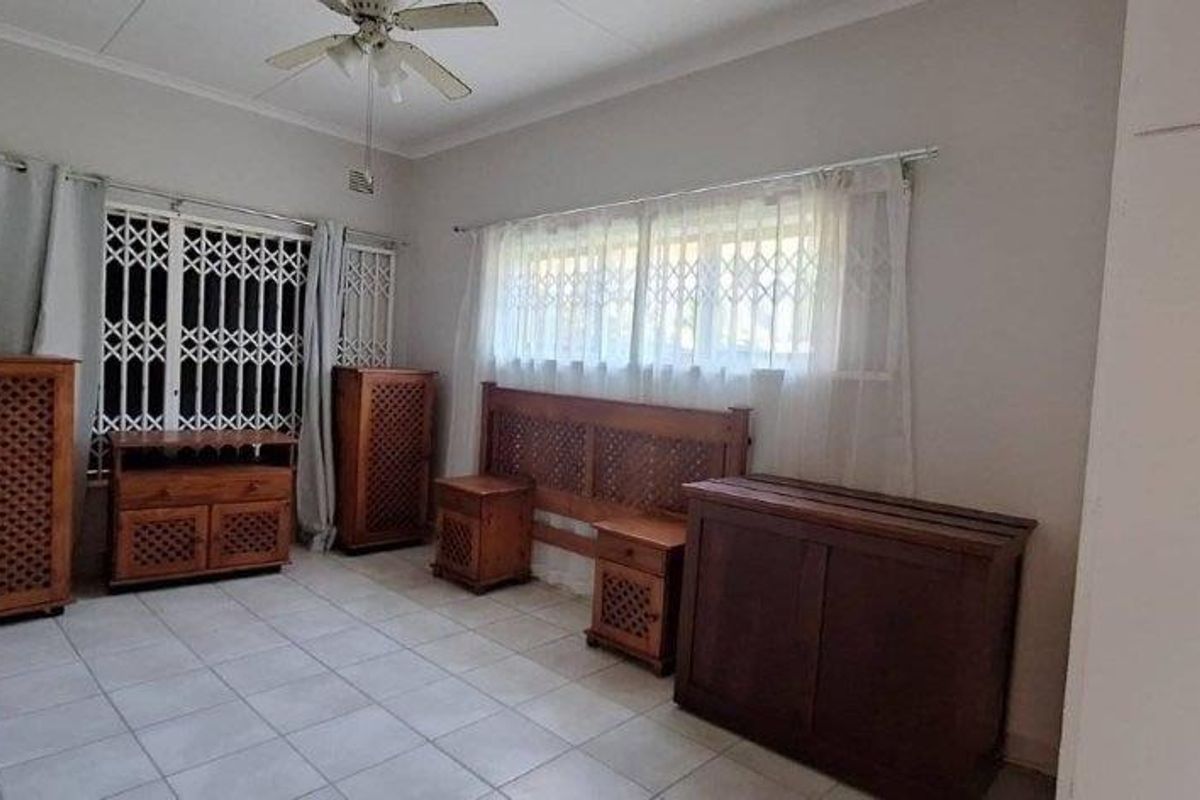 A bedroom featuring tiled flooring, built-in cupboards, a ceiling fan, and security gates on the windows.