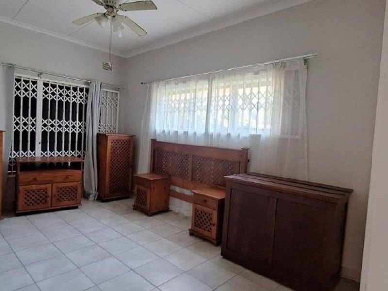 A bedroom featuring tiled flooring, built-in cupboards, a ceiling fan, and security gates on the windows.