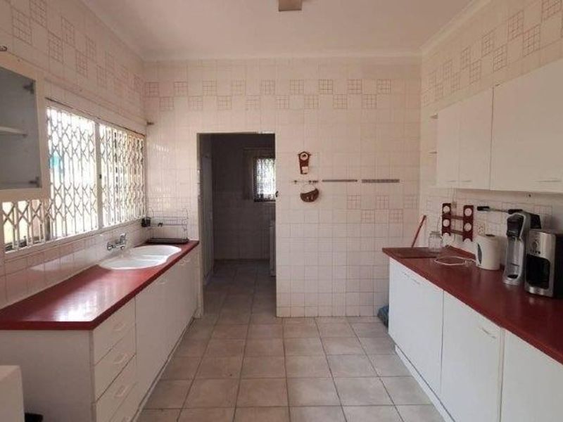 A functional kitchen featuring white cabinetry, red countertops, tiled walls, and a double basin sink with security bars on the window.