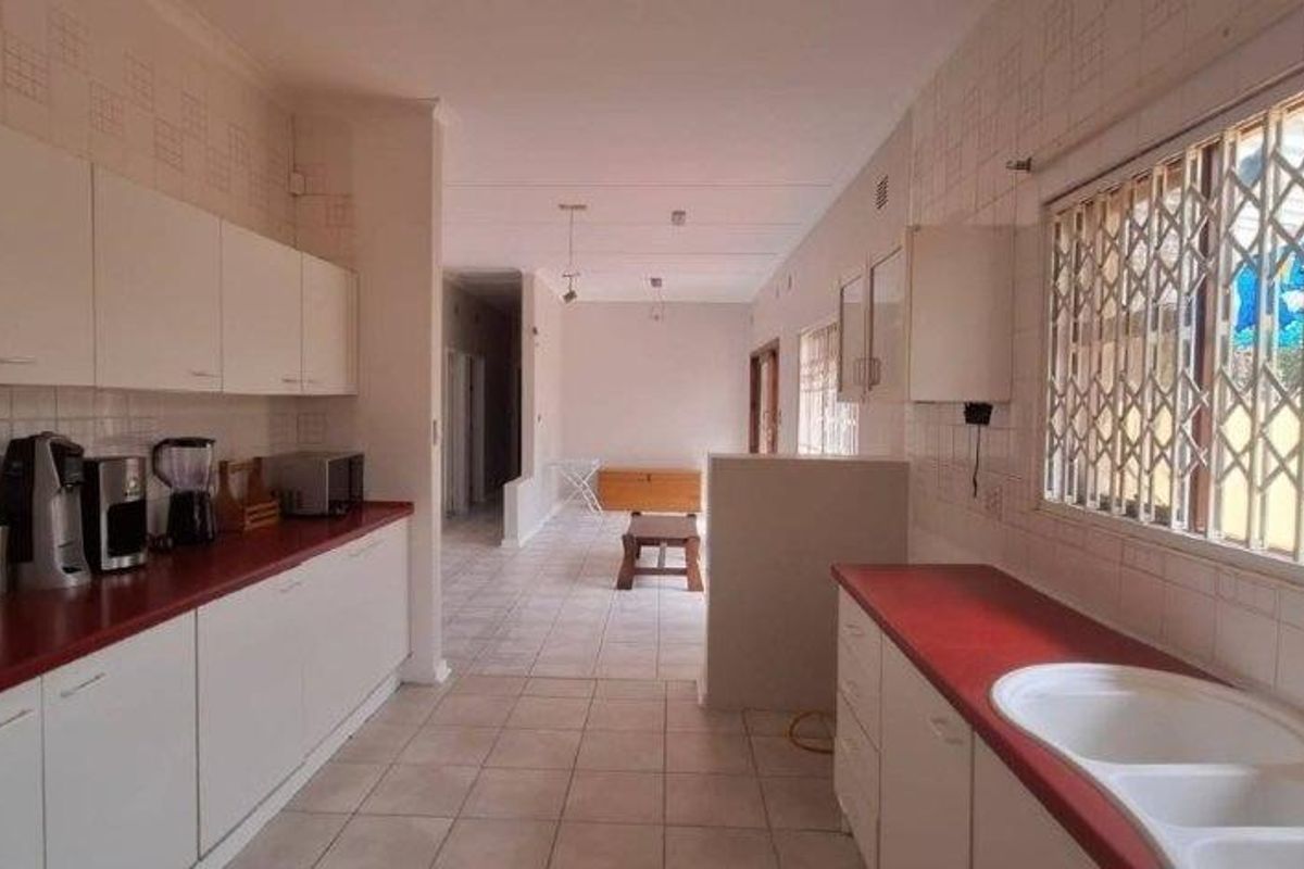 Spacious kitchen featuring extensive white cabinetry, laminate countertops, double basin sink, and tiled flooring, offering a functional layout with potential for modern updates.