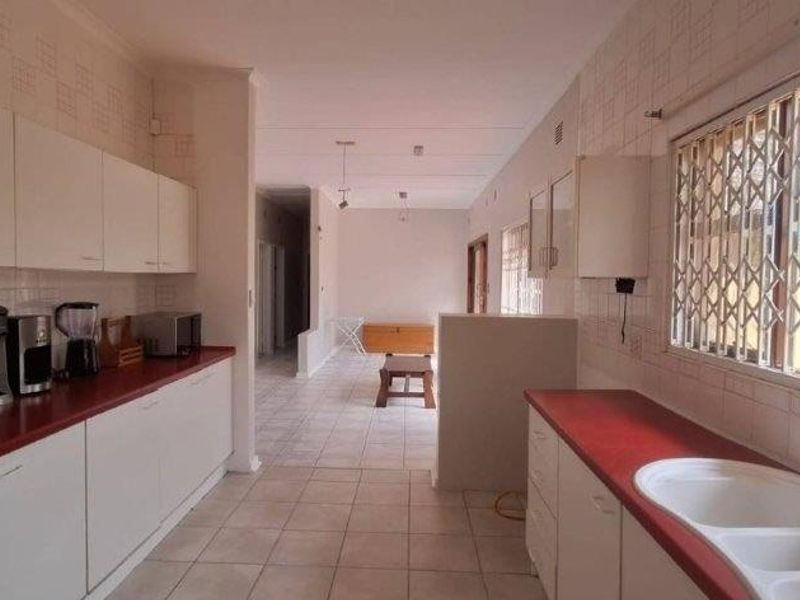 Spacious kitchen featuring extensive white cabinetry, laminate countertops, double basin sink, and tiled flooring, offering a functional layout with potential for modern updates.