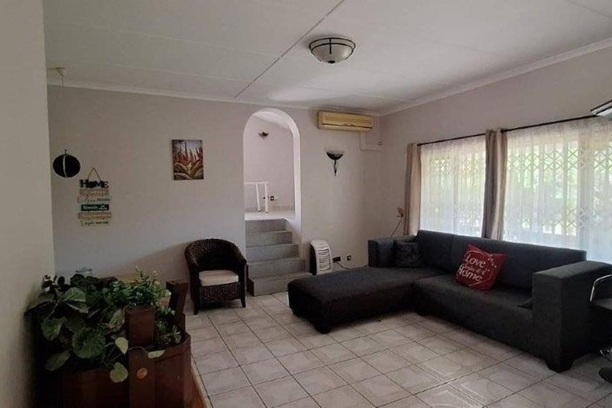 A living room featuring tiled flooring, an arched entryway, and a wall-mounted air conditioning unit, offering a functional and neutral living space.