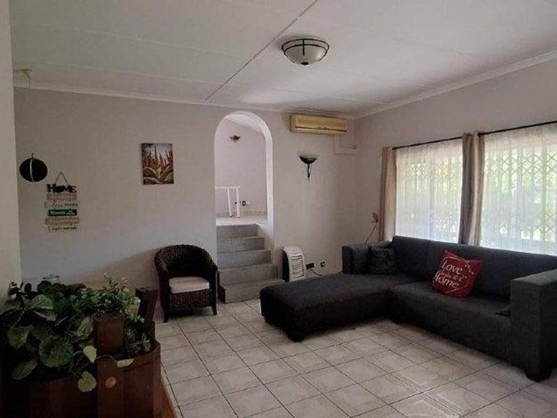 A living room featuring tiled flooring, an arched entryway, and a wall-mounted air conditioning unit, offering a functional and neutral living space.