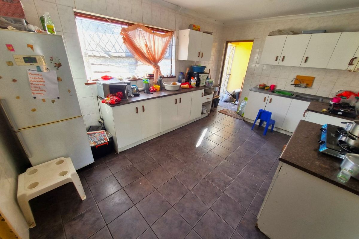 A functional kitchen featuring tiled flooring, ample built-in cabinetry, laminate countertops, and a stainless steel sink, offering potential for modernization.