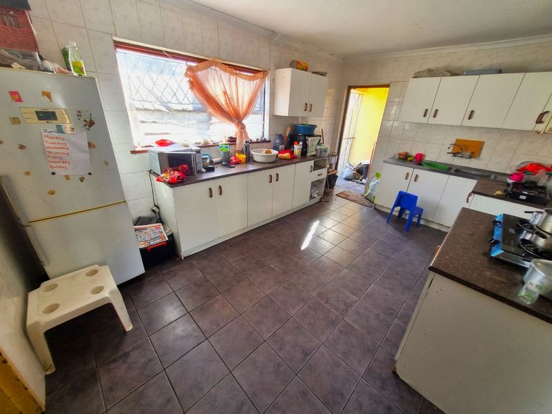 A functional kitchen featuring tiled flooring, ample built-in cabinetry, laminate countertops, and a stainless steel sink, offering potential for modernization.