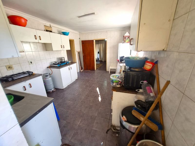 A functional kitchen featuring tiled walls and flooring, built-in cabinetry, and a gas hob, offering potential for modernization and cosmetic updates.