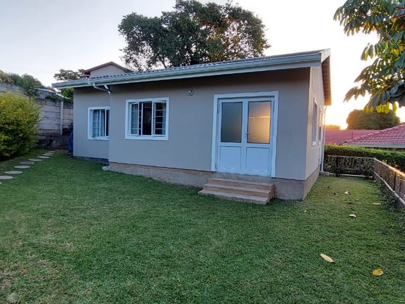 Rear view of the property featuring a well-maintained lawn, stone pathway, and access via double glass doors.