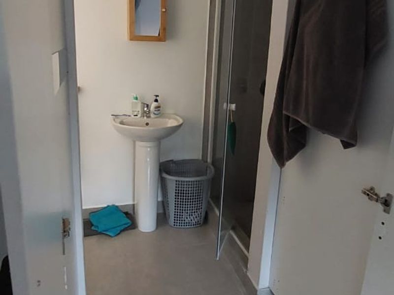 A functional bathroom featuring a pedestal sink, a shower enclosure with glass door, and neutral floor tiling.