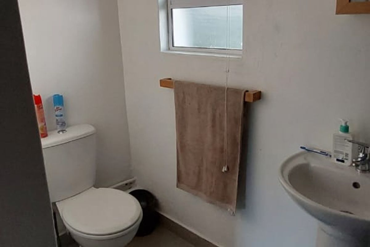 A functional bathroom featuring a pedestal basin, standard toilet, and a top-hung window with neutral floor tiling.