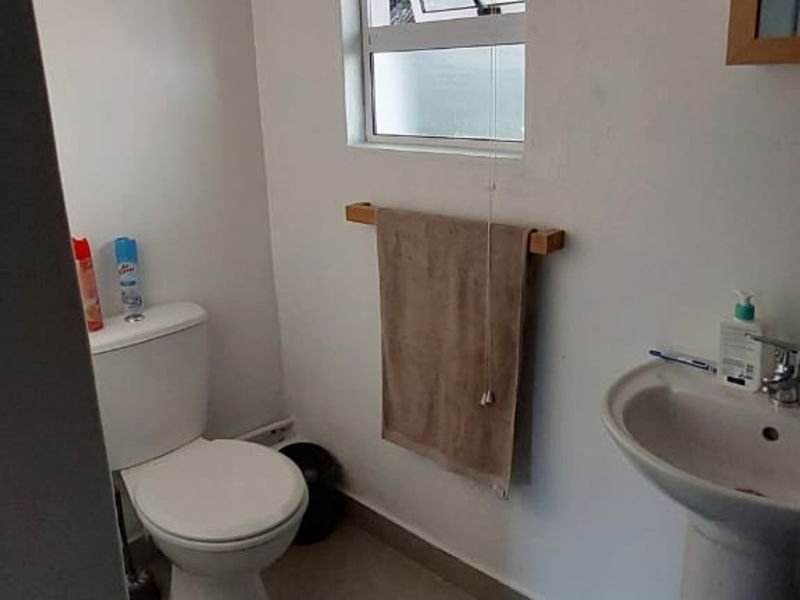 A functional bathroom featuring a pedestal basin, standard toilet, and a top-hung window with neutral floor tiling.