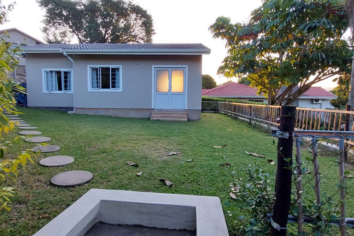 A view of the rear exterior of the apartment featuring a well-maintained lawn, concrete stepping stones, a fire pit, and secure perimeter fencing.