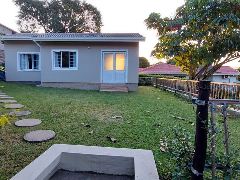 A view of the rear exterior of the apartment featuring a well-maintained lawn, concrete stepping stones, a fire pit, and secure perimeter fencing.