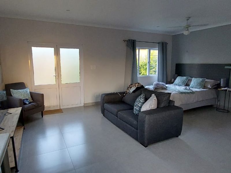 An open-plan living and bedroom area featuring neutral tiled flooring, a ceiling fan, and direct access to an outdoor space via double glass doors.