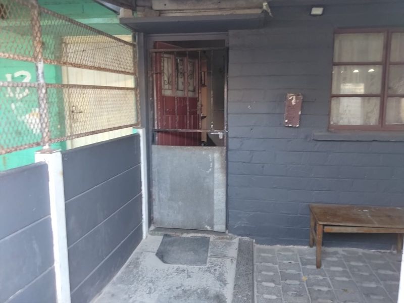 Front entrance area featuring a security gate, brick facade, and paved flooring, showing signs of wear and weathering.