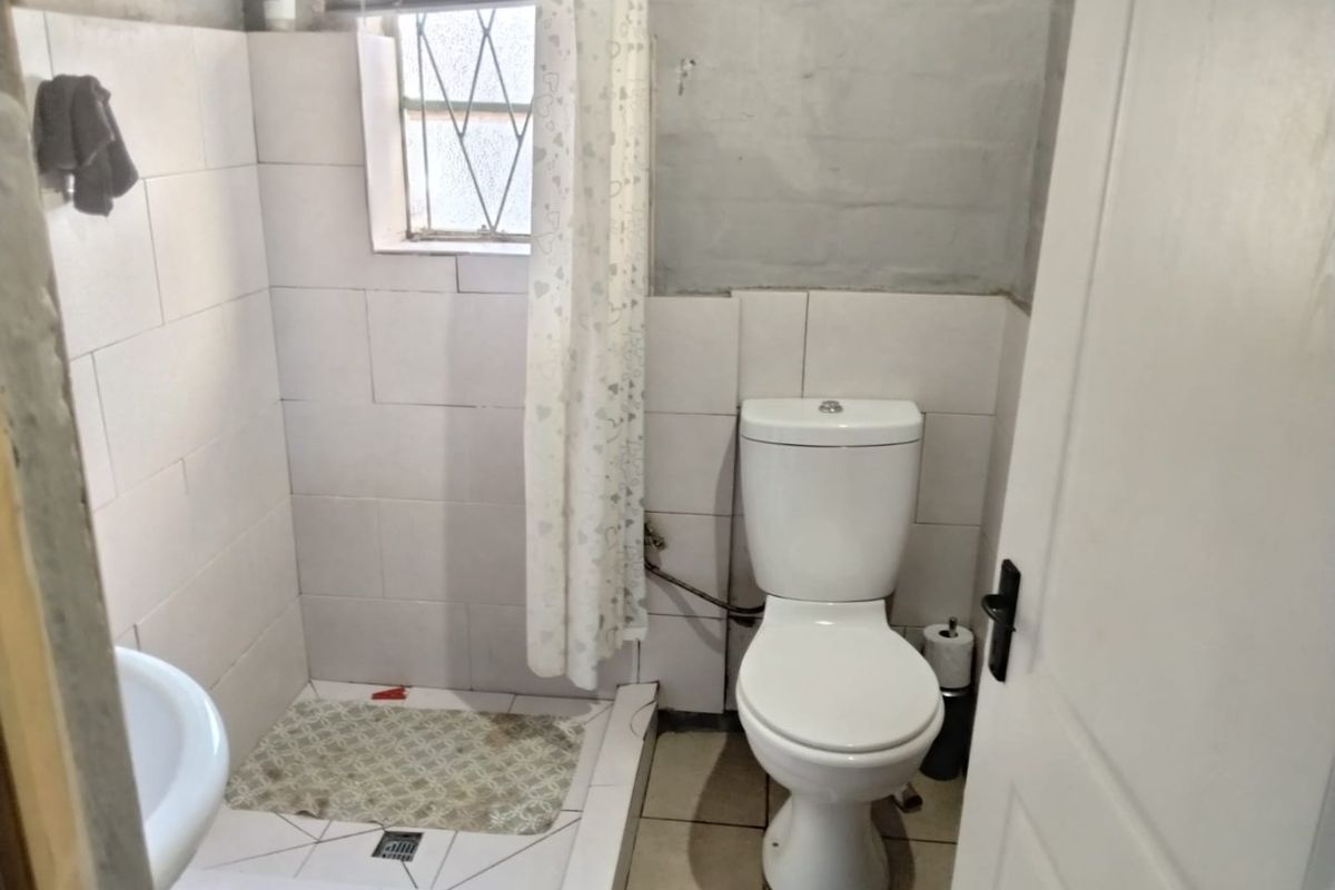 A compact bathroom featuring a toilet, shower cubicle, and basin, with tiled finishes requiring some maintenance and cosmetic updates.
