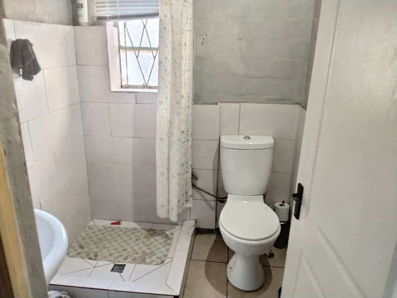 A compact bathroom featuring a toilet, shower cubicle, and basin, with tiled finishes requiring some maintenance and cosmetic updates.